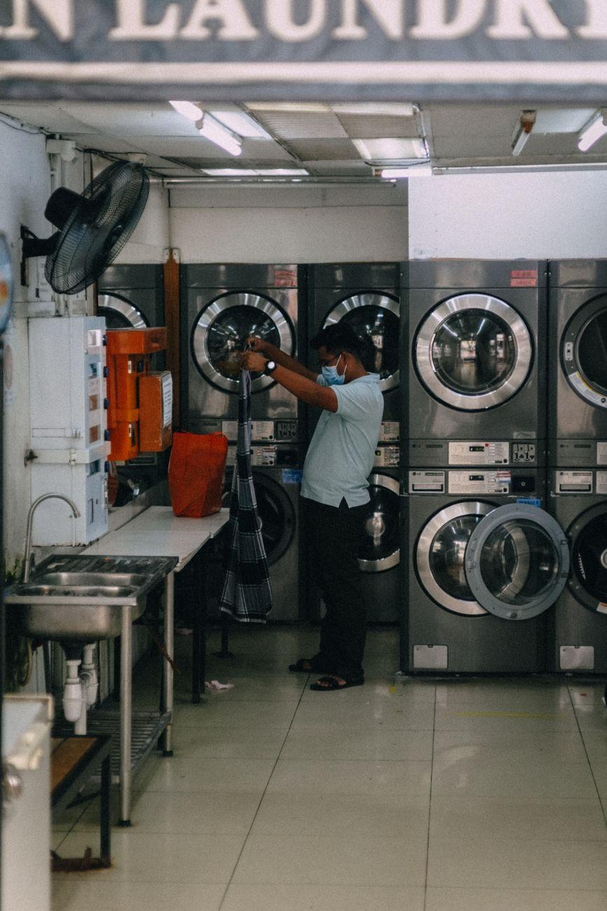 Man organizing laundry in a laundromat with washing machines and a bright interior.