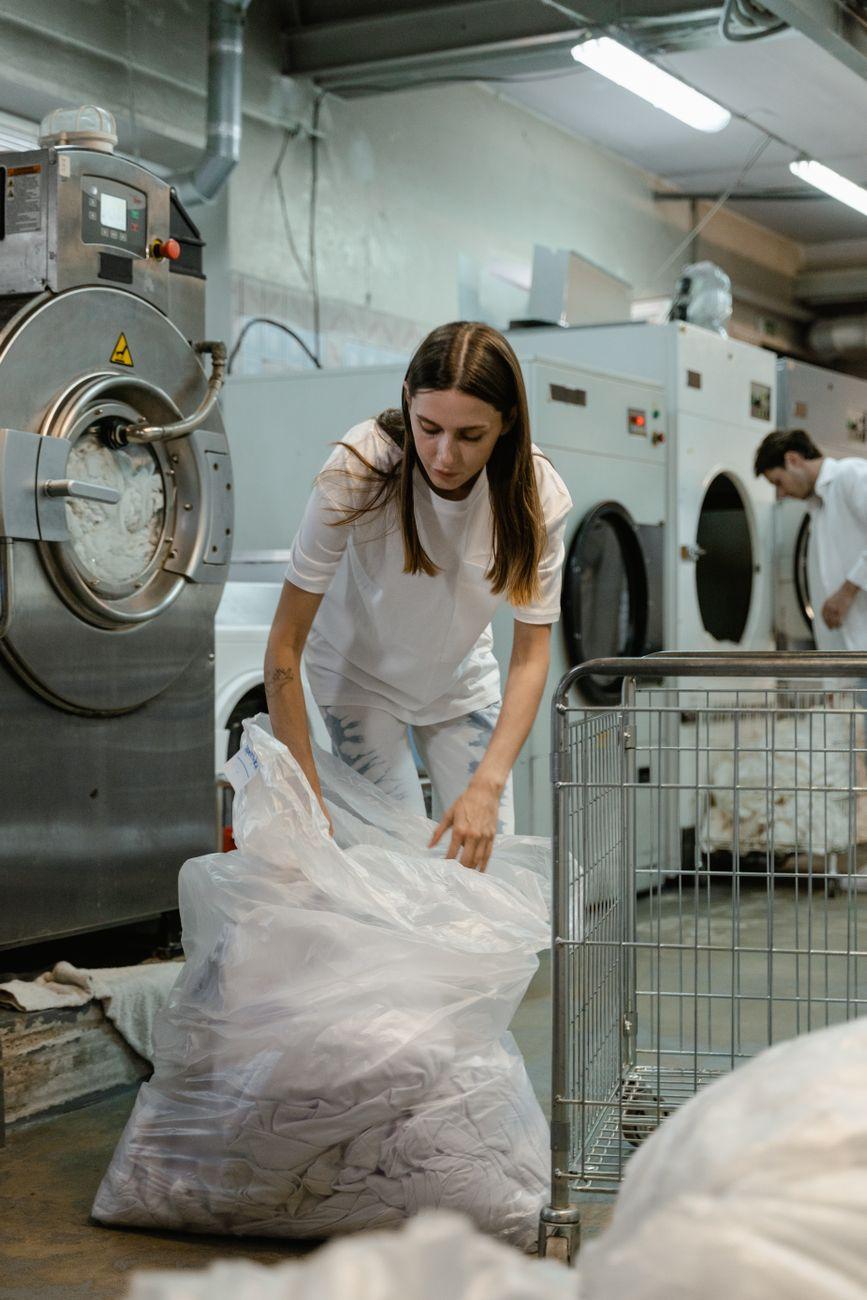 Woman handling laundry in a commercial washing facility, focusing on tasks and efficiency.