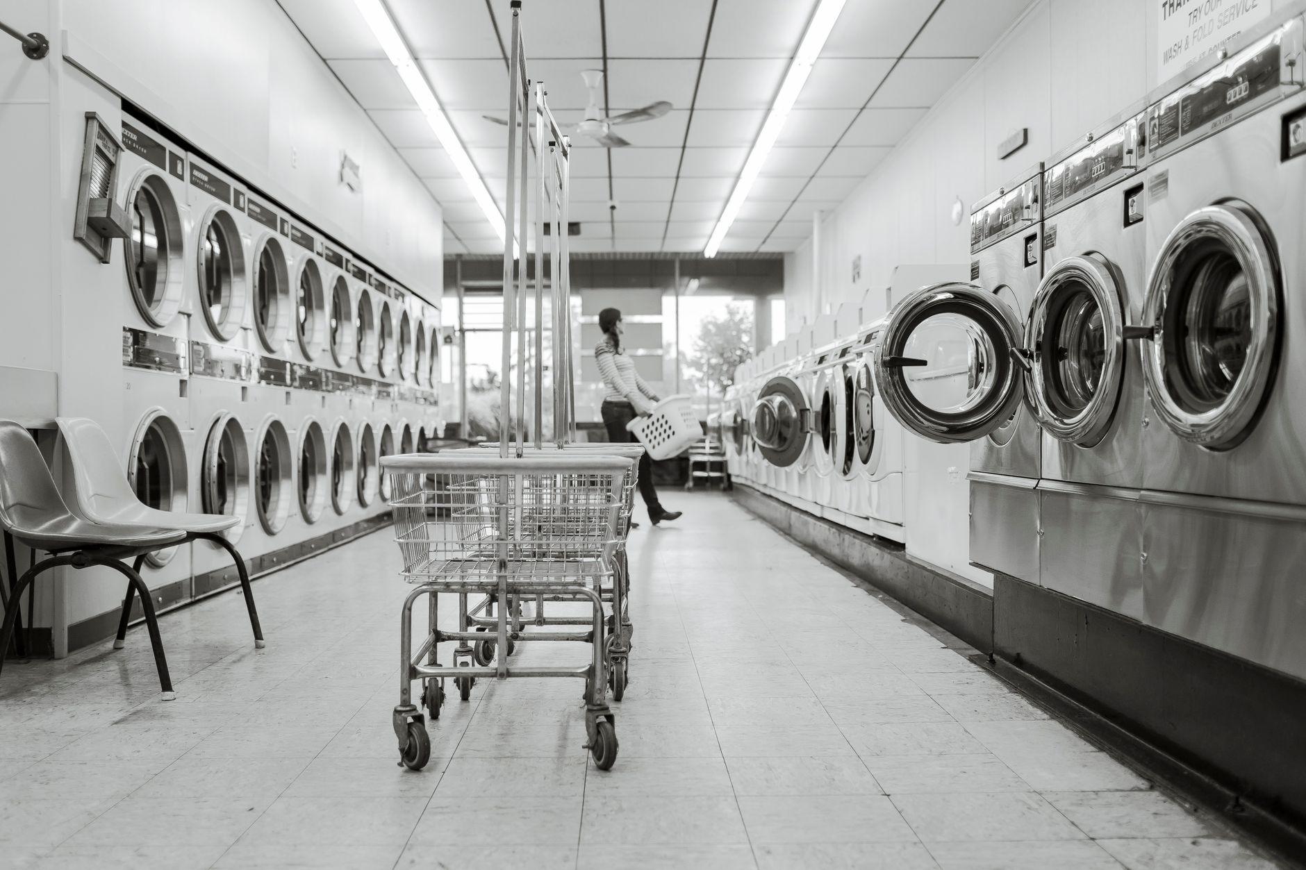 Black and white image of a laundromat with laundry machines and a person in the background.